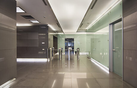 Commercial office lift hall with glass walls, polished stone flooring, recessed lighting, and modern elevator design.