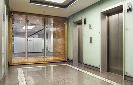 Commercial office lift hall with glass walls, polished stone flooring, recessed lighting, and modern elevator design.